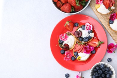 Photo of Sweet tartlets with berries and flowers on light grey table, flat lay with space for text. Delicious dessert