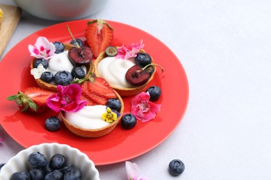 Photo of Sweet tartlets with berries and flowers on light grey table, closeup with space for text. Delicious dessert