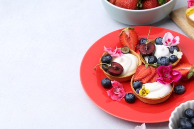 Photo of Sweet tartlets with berries and flowers on light grey table, closeup with space for text. Delicious dessert