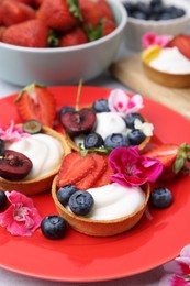Photo of Sweet tartlets with berries and flowers on grey table, closeup. Delicious dessert