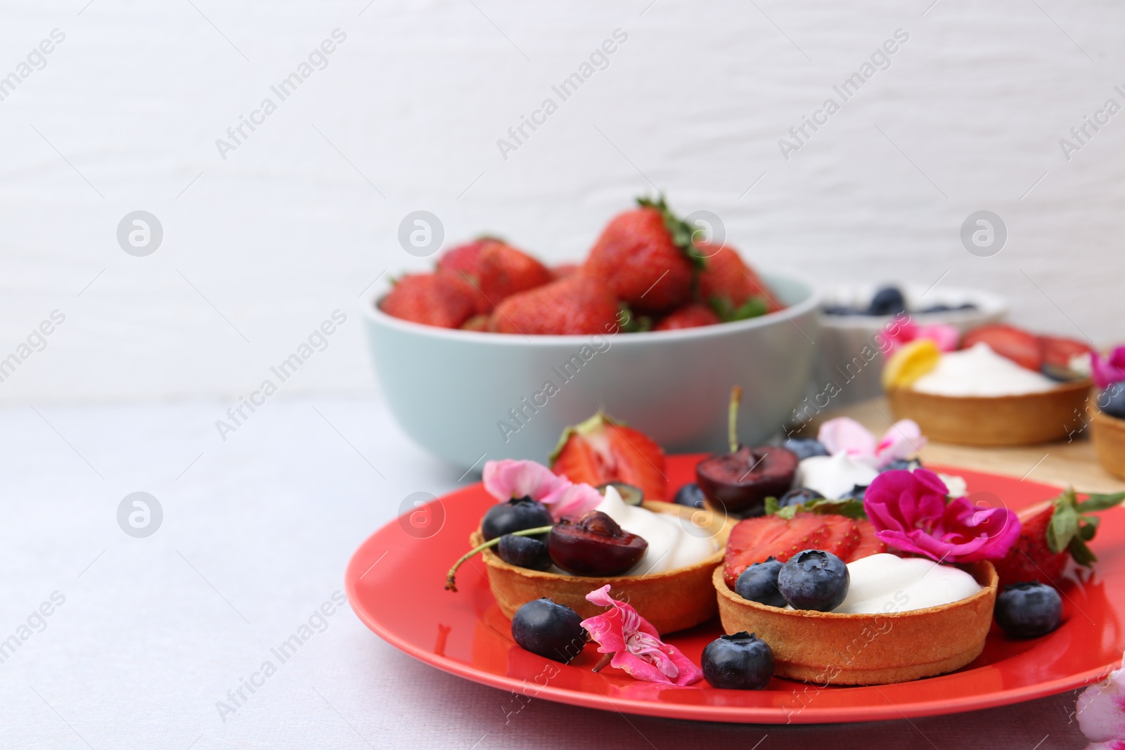 Sweet tartlets with berries and flowers on light table, closeup with space for text. Delicious dessert Photo of Sweet tartlets with berries and flowers on light table, closeup with space for text. Delicious dessert
