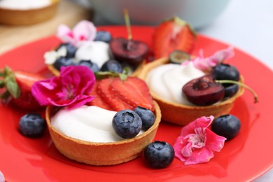 Photo of Sweet tartlets with berries and flowers on light table, closeup. Delicious dessert