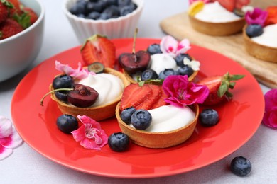 Photo of Sweet tartlets with berries and flowers on grey table, closeup. Delicious dessert