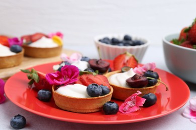 Photo of Sweet tartlets with berries and flowers on grey table against light background, closeup. Delicious dessert