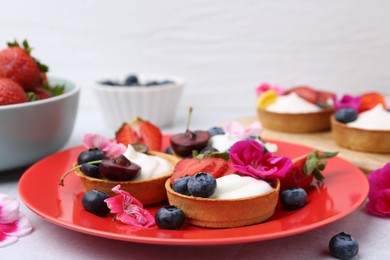 Photo of Sweet tartlets with berries and flowers on grey table against light background, closeup. Delicious dessert