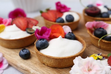 Photo of Sweet tartlets with berries and flowers on grey table, closeup. Delicious dessert