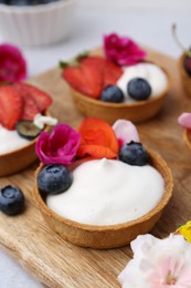 Photo of Sweet tartlets with berries and flowers on grey table, closeup. Delicious dessert