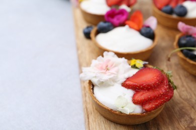 Photo of Sweet tartlets with berries and flowers on light table, closeup with space for text. Delicious dessert