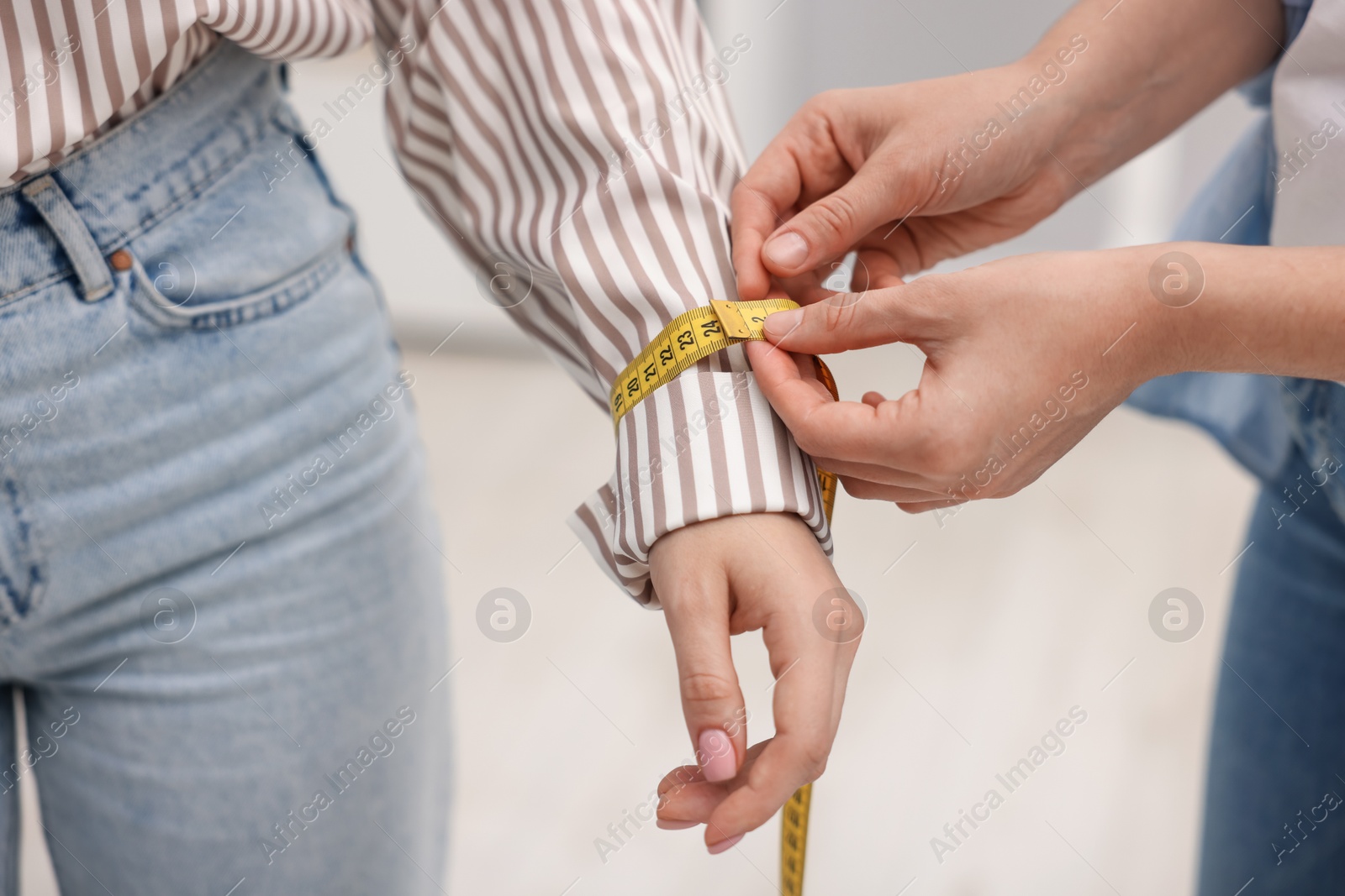 Photo of Tailor measuring woman's wrist with tape in atelier, closeup
