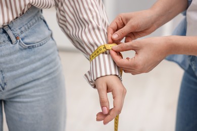 Photo of Tailor measuring woman's wrist with tape in atelier, closeup