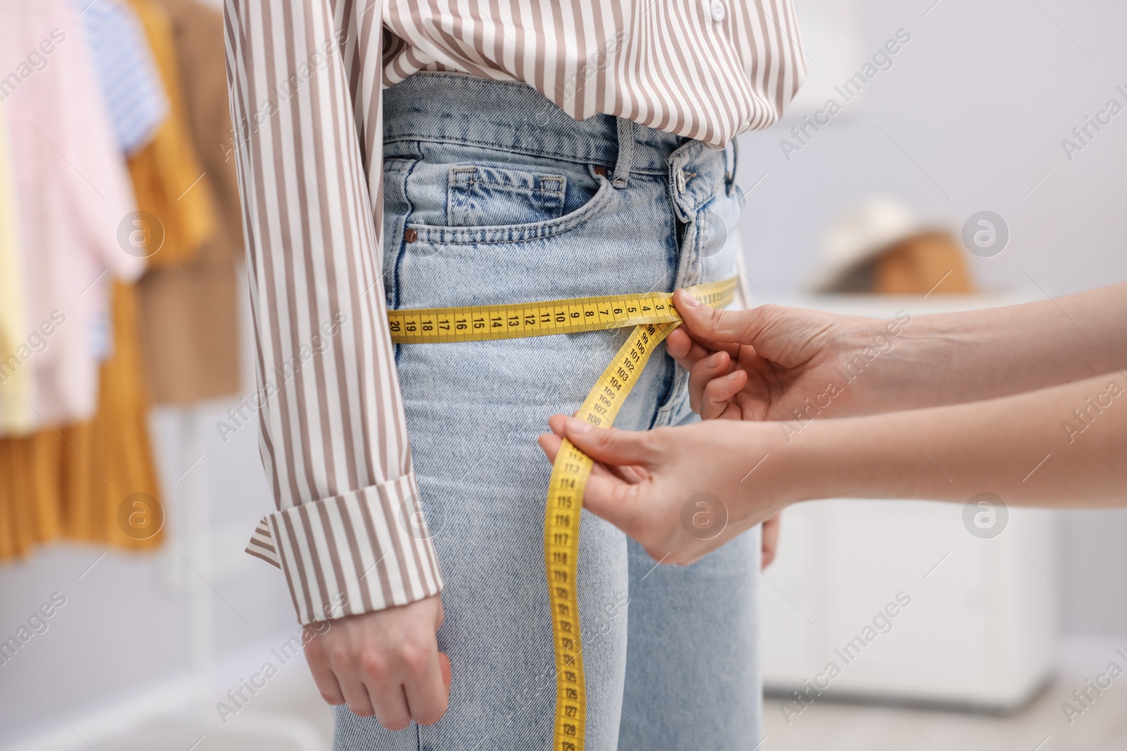 Photo of Tailor measuring woman's hips in atelier, closeup