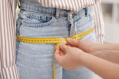 Photo of Tailor measuring woman's hips in atelier, closeup
