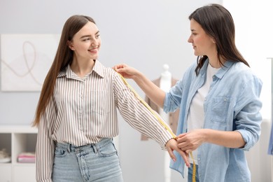 Photo of Tailor measuring woman's arm with tape in atelier