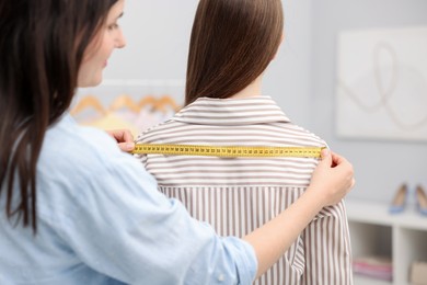 Photo of Tailor measuring woman's back in atelier, closeup
