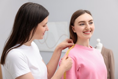 Photo of Tailor measuring woman's shoulder with tape in atelier