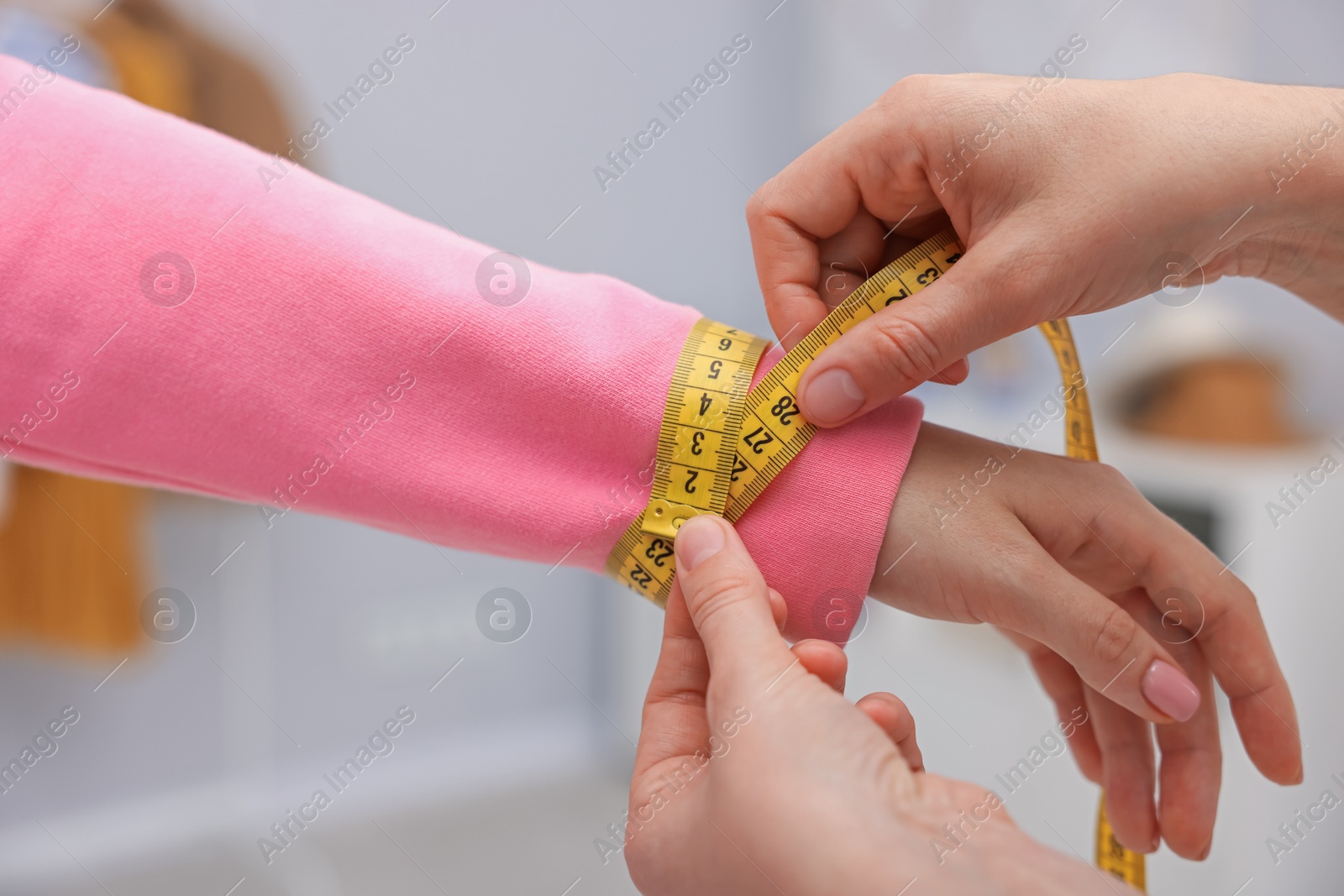 Photo of Tailor measuring woman's wrist with tape in atelier, closeup