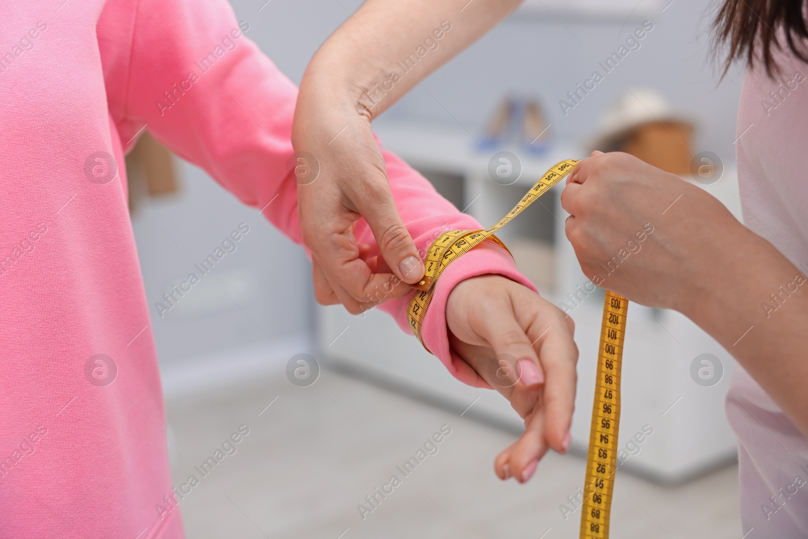 Photo of Tailor measuring woman's wrist with tape in atelier, closeup