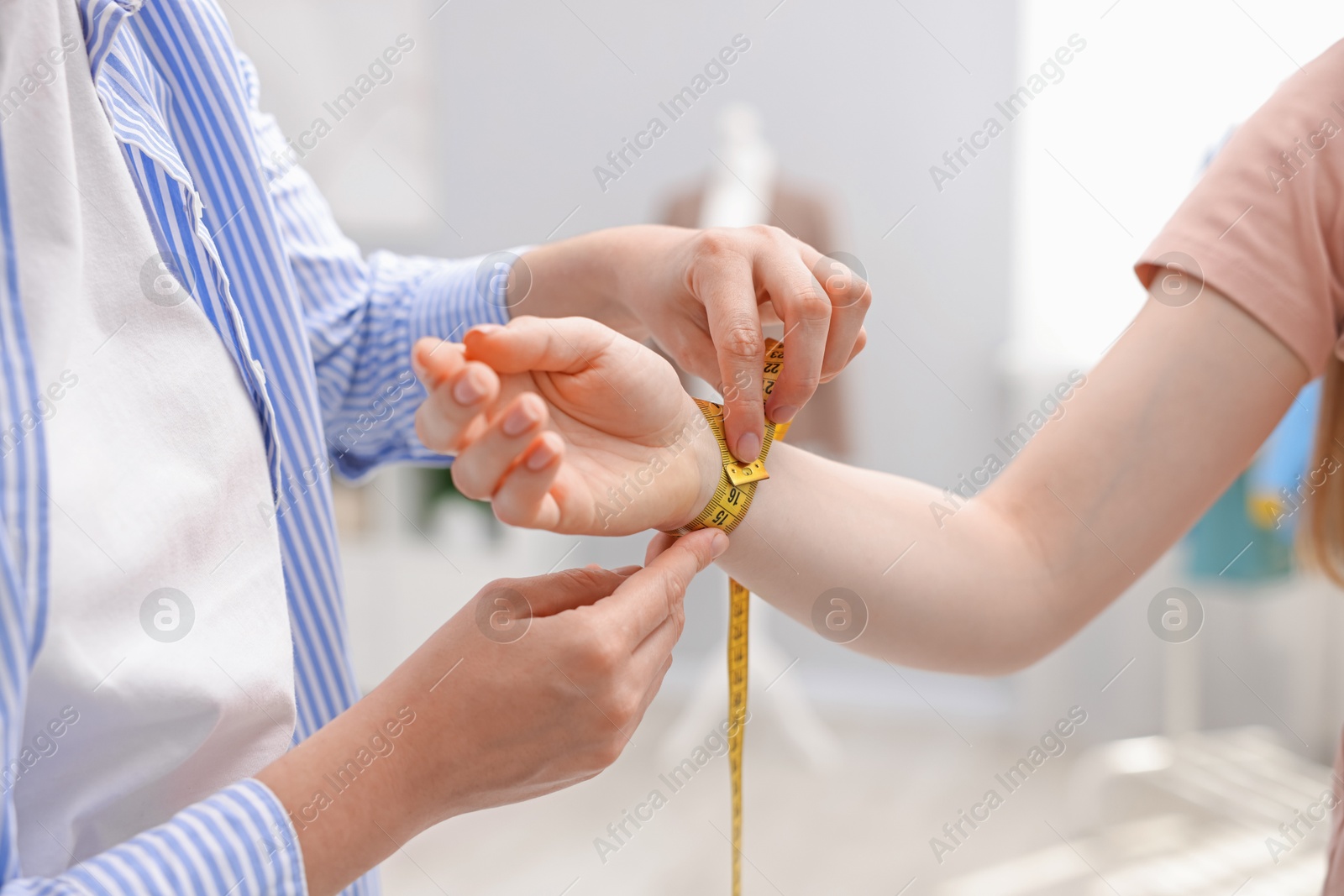 Photo of Tailor measuring woman's wrist with tape in atelier, closeup