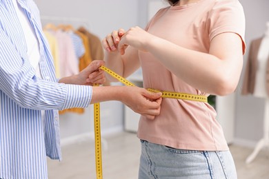 Photo of Tailor measuring woman's waist with tape in atelier, closeup