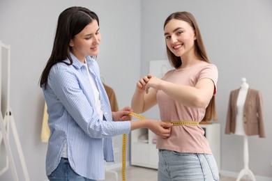 Photo of Tailor measuring woman's waist with tape in atelier