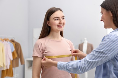 Photo of Tailor measuring woman's chest with tape in atelier