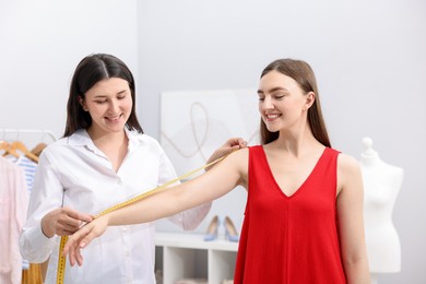 Photo of Tailor measuring woman's arm with tape in atelier