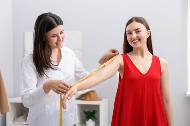 Photo of Tailor measuring woman's arm with tape in atelier