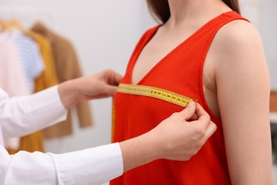 Photo of Tailor measuring woman's chest with tape in atelier, closeup