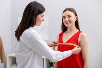 Photo of Tailor measuring woman's chest with tape in atelier