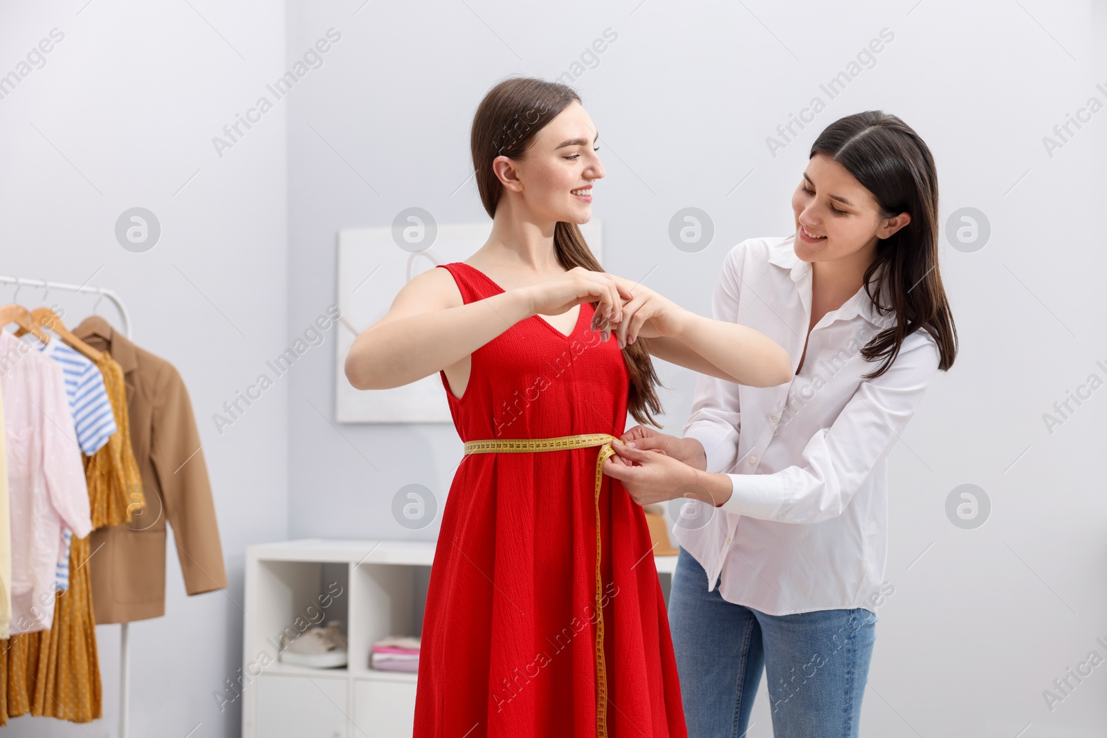 Photo of Tailor measuring woman's waist with tape in atelier