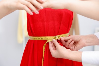 Photo of Tailor measuring woman's waist with tape in atelier, closeup