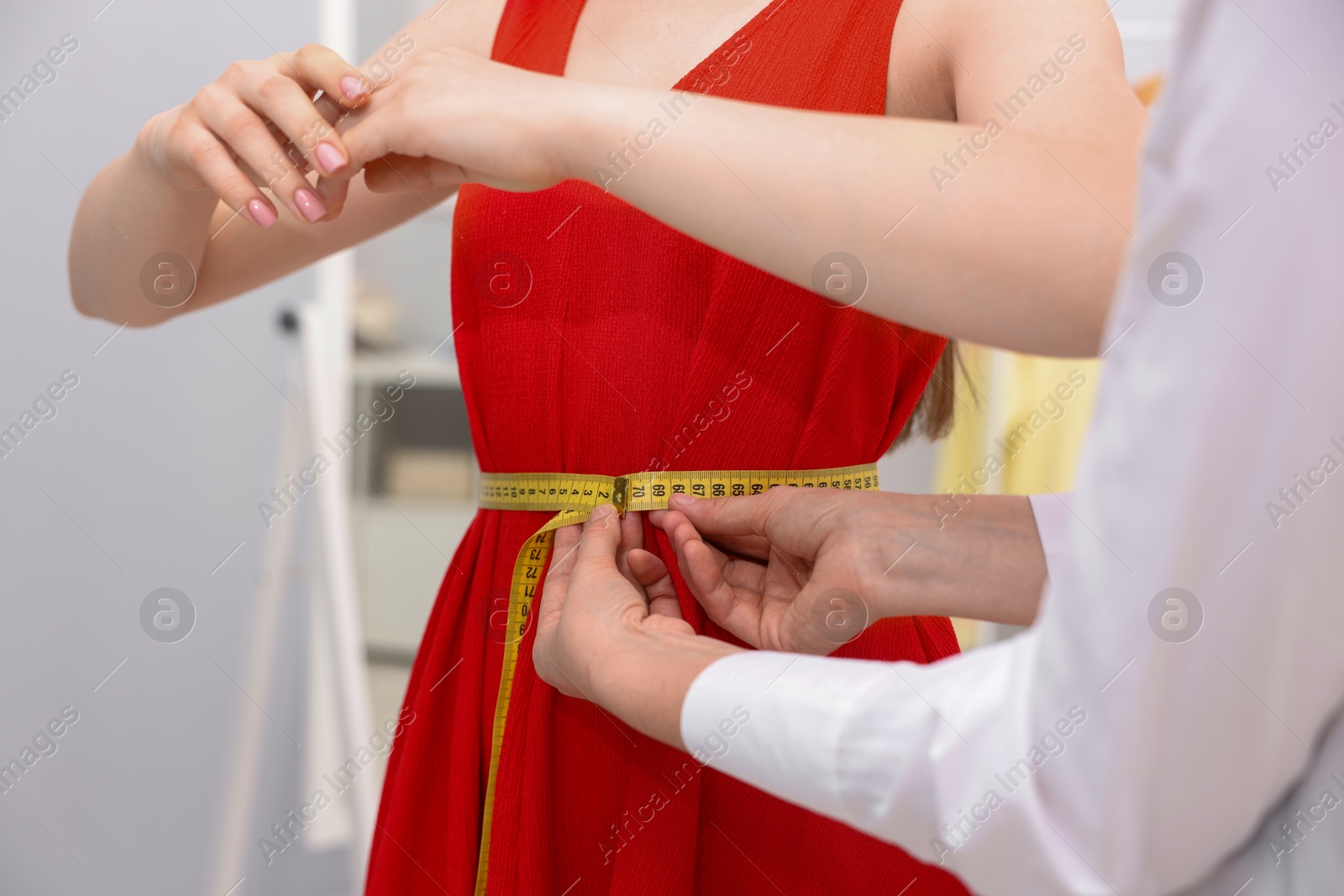 Photo of Tailor measuring woman's waist with tape in atelier, closeup