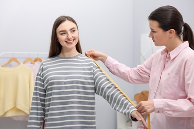 Photo of Tailor measuring woman's arm with tape in atelier