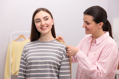 Photo of Tailor measuring woman's shoulder with tape in atelier