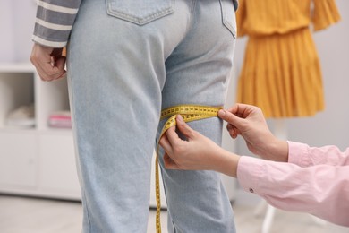 Photo of Tailor measuring woman's leg with tape in atelier, closeup