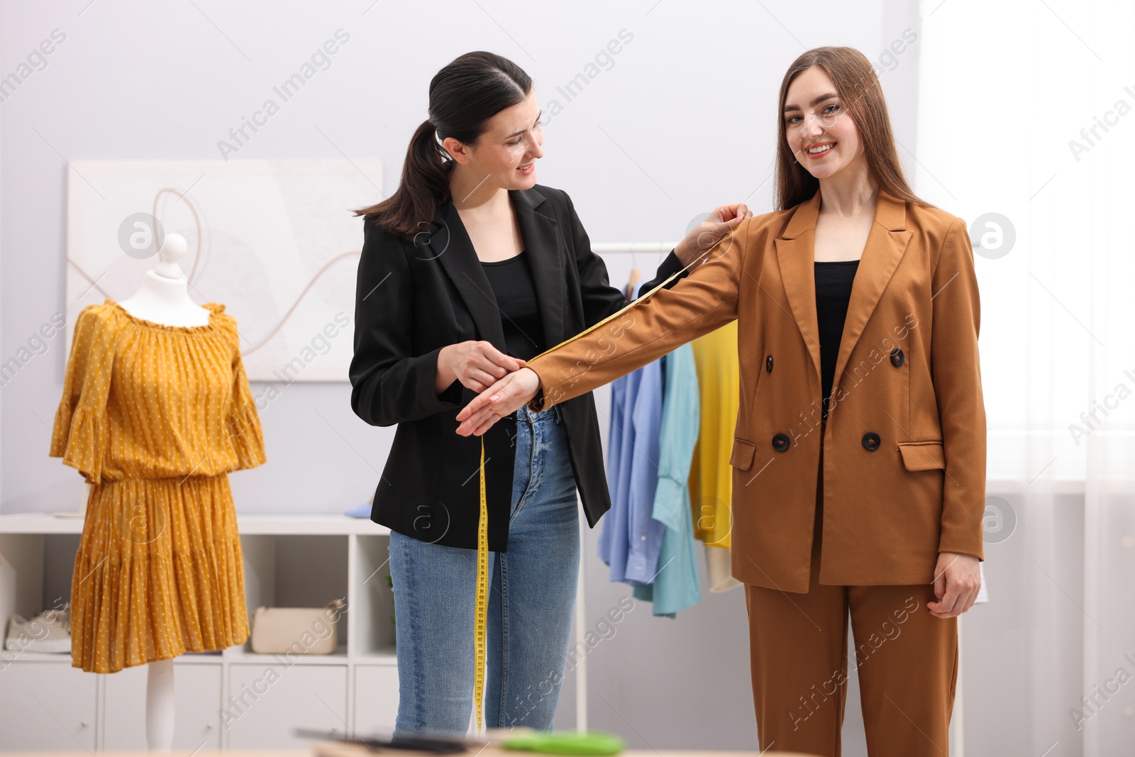 Photo of Tailor measuring jacket sleeve on woman in atelier