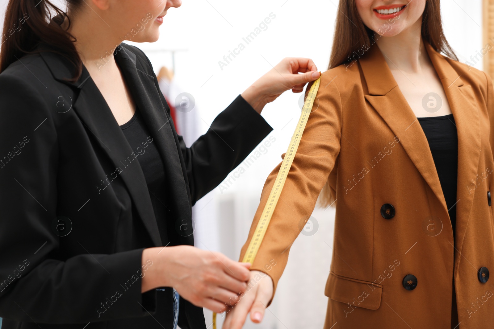 Photo of Tailor measuring jacket sleeve on woman in atelier, closeup