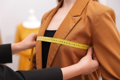 Photo of Tailor measuring jacket on woman in atelier, closeup