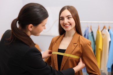 Photo of Tailor measuring jacket on woman in atelier