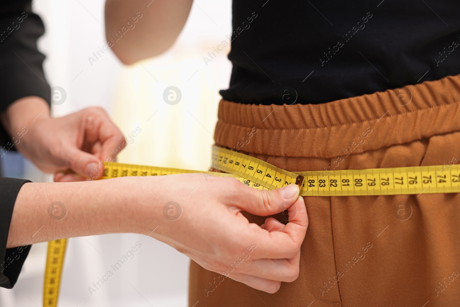 Photo of Tailor measuring pants on woman in atelier, closeup