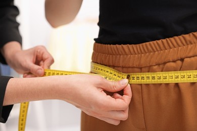 Photo of Tailor measuring pants on woman in atelier, closeup