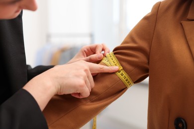 Photo of Tailor measuring jacket sleeve on woman in atelier, closeup