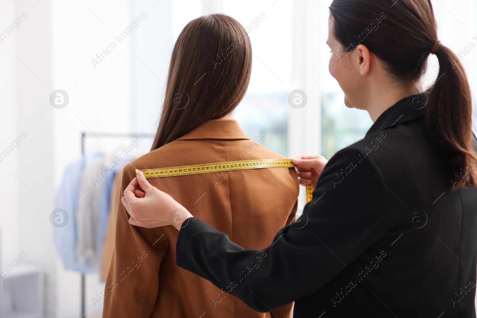 Tailor measuring jacket on woman in atelier, back view Photo of Tailor measuring jacket on woman in atelier, back view