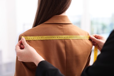 Photo of Tailor measuring jacket on woman in atelier, closeup