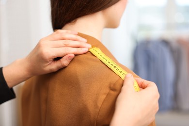 Photo of Tailor measuring jacket on woman in atelier, closeup