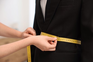 Photo of Tailor measuring jacket on man in atelier, closeup