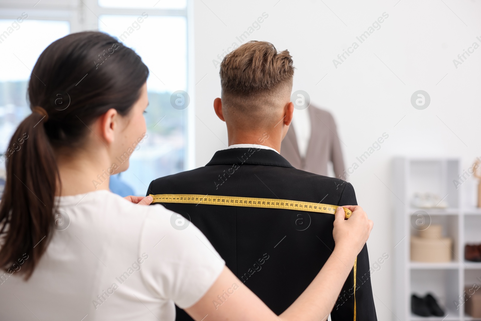 Photo of Tailor measuring jacket on man in atelier, back view