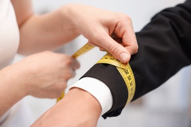 Photo of Tailor measuring jacket on man in atelier, closeup