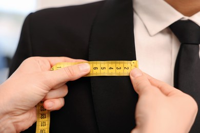 Photo of Tailor measuring jacket on man in atelier, closeup