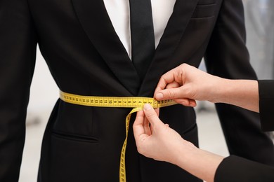 Photo of Tailor measuring jacket on man in atelier, closeup